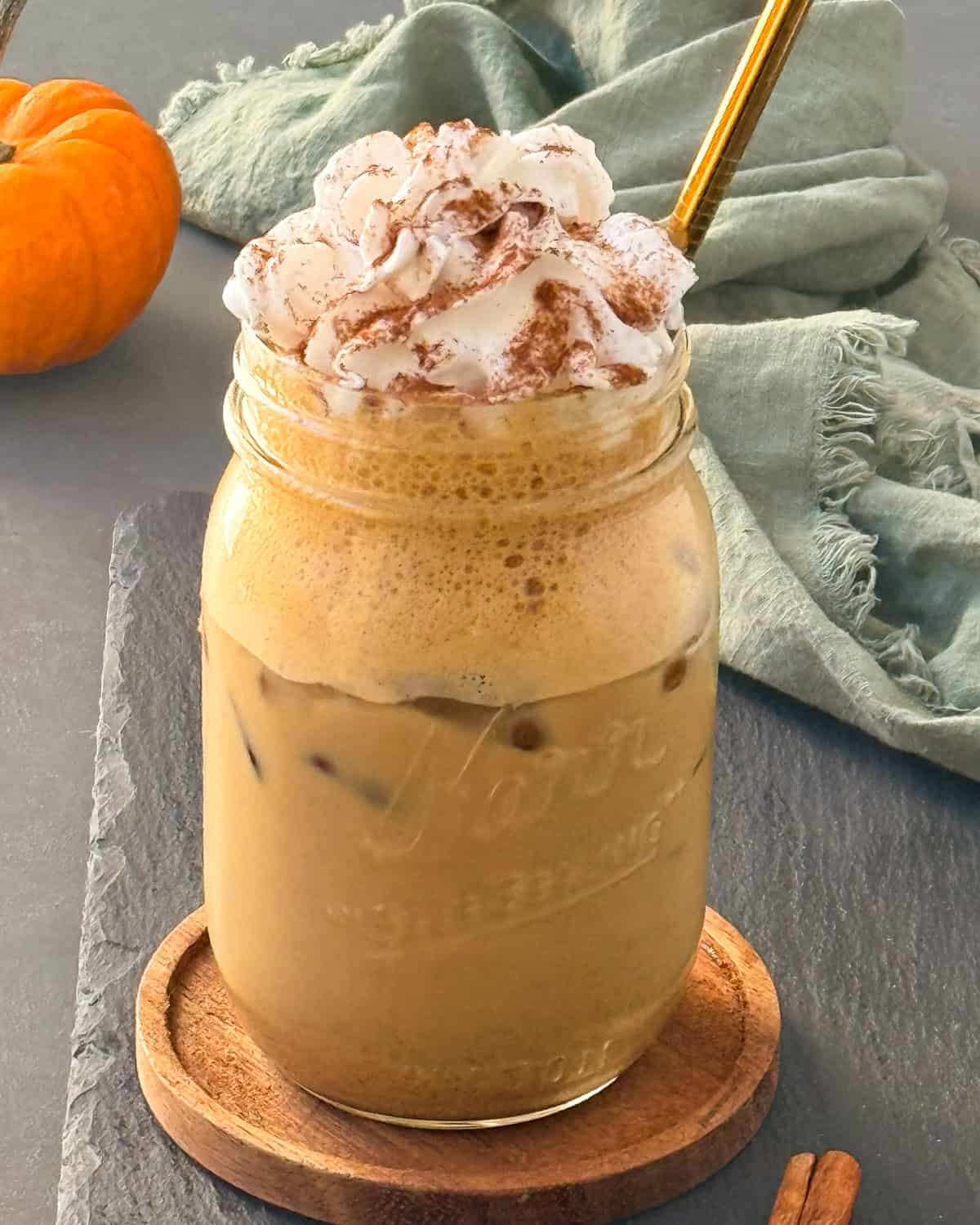 Iced pumpkin spice latte in a mason jar, topped with whipped cream and a sprinkle of cinnamon powder.