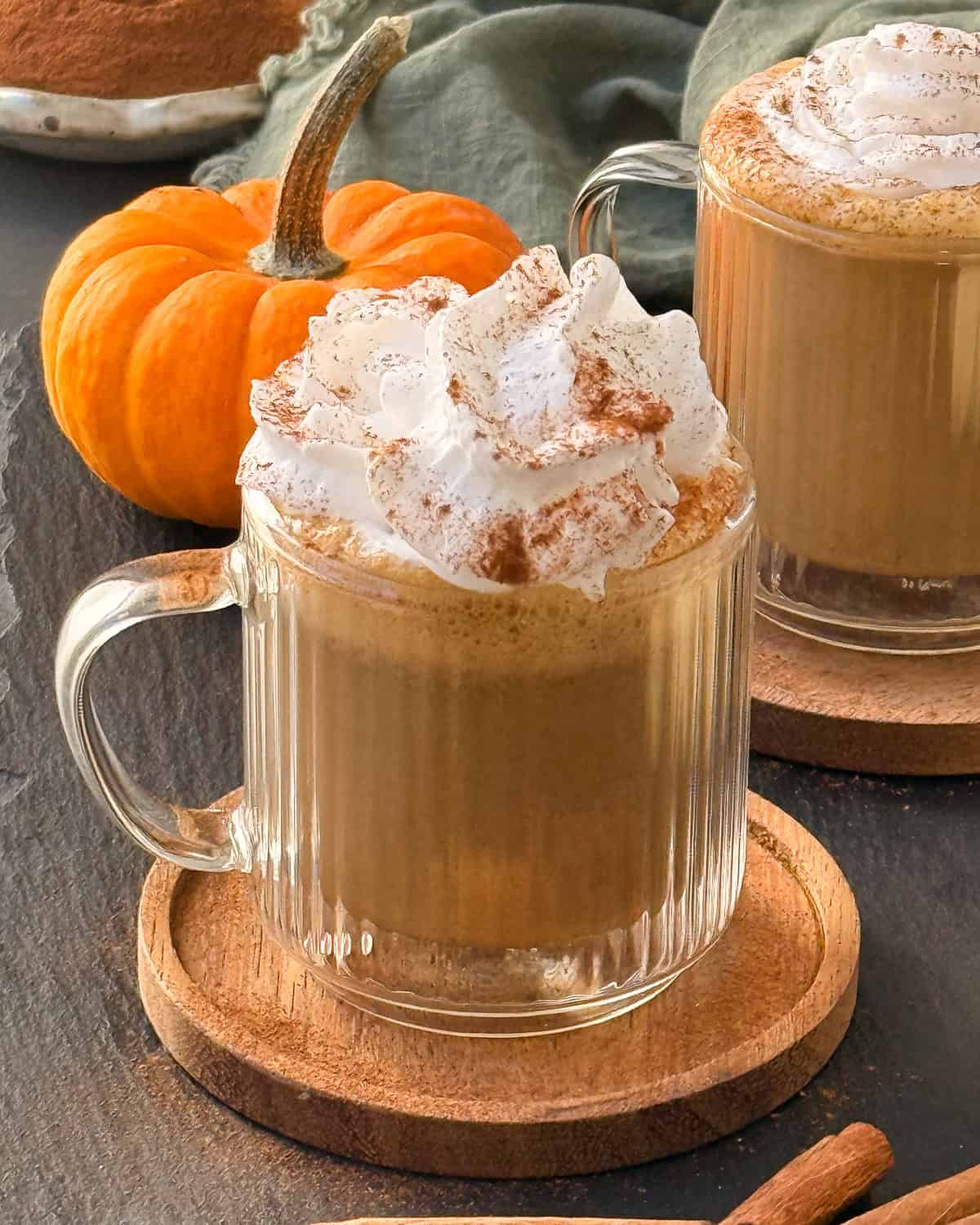 A couple of glass mugs with vegan pumpkin spice latte, topped with whipped cream and a sprinkle of cinnamon powder.