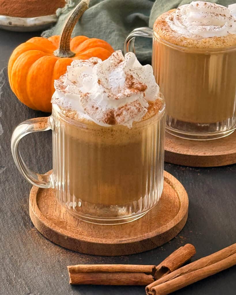 Pumpkin spice latte in two glass cups topped with whipped cream and a sprinkle of cinnamon.