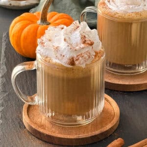 Vegan pumpkin spice latte in a glass mug, topped with whipped cream and a sprinkle of cinnamon powder.