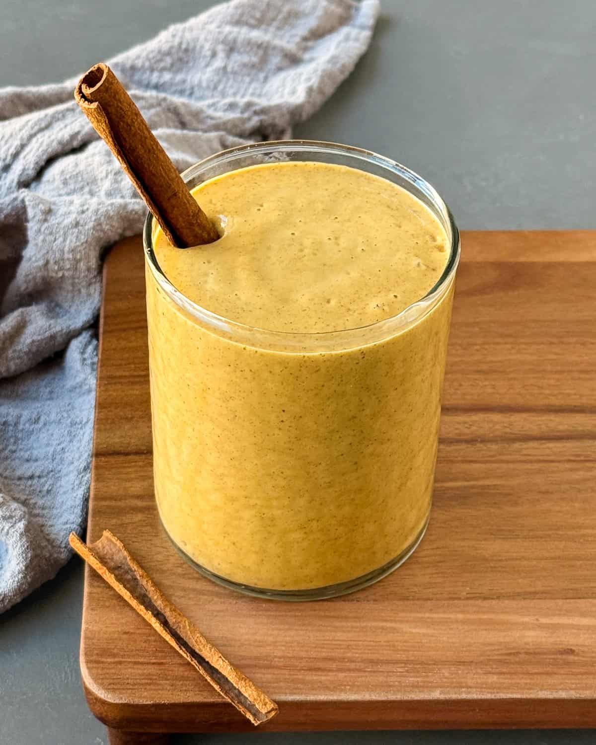 Pumpkin pie protein shake in a glass with a cinnamon stick inserted in it.
