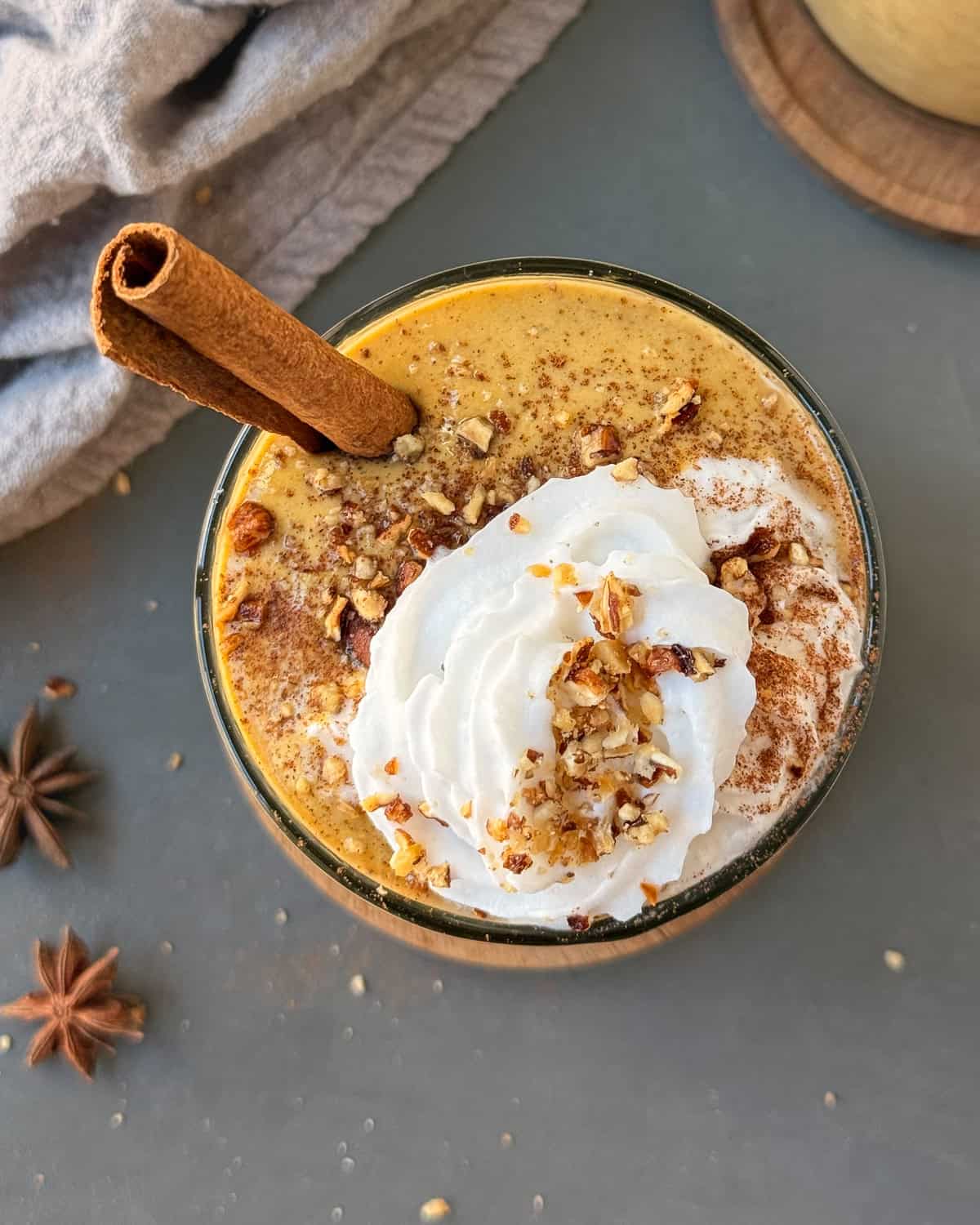 Pumpkin spice protein shake in a glass topped with whip cream, cinnamon, crushed pecans, and a cinnamon stick.
