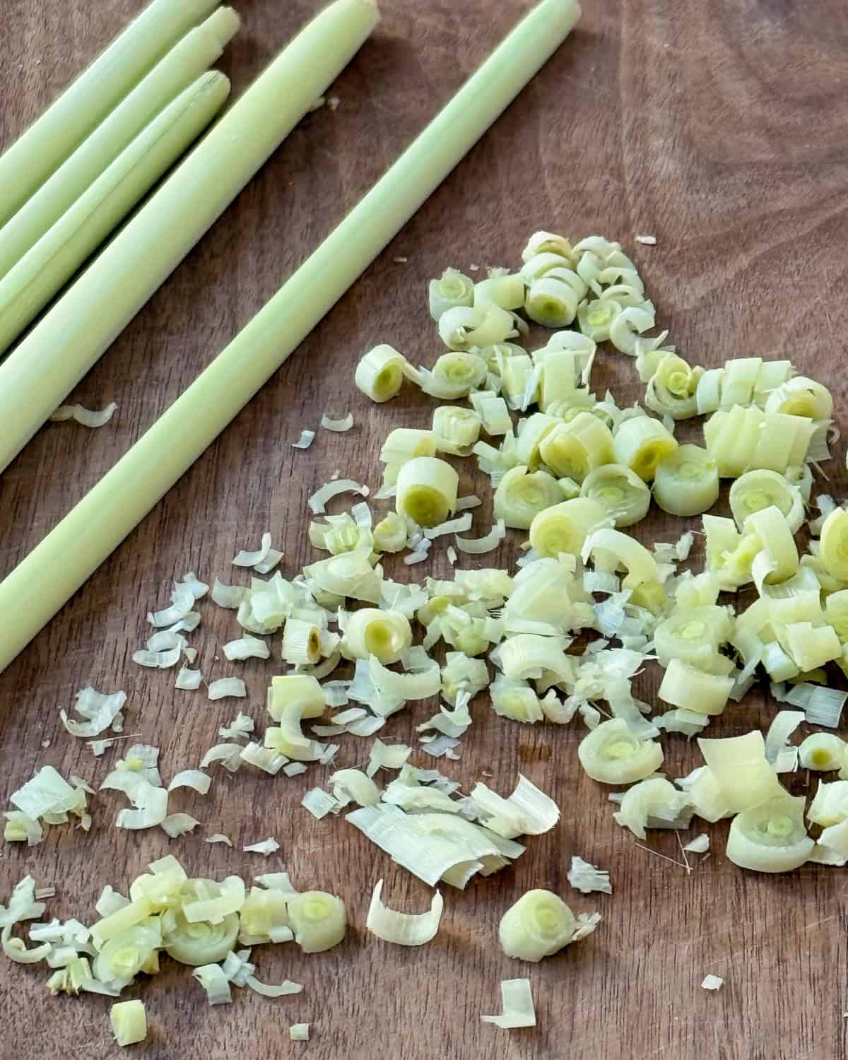 Thinly sliced lemongrass on a wooden cutting board.
