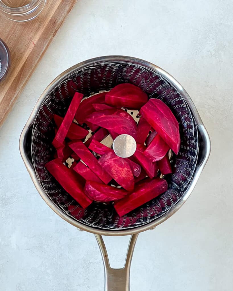 Sliced beets in a pot over a steaming basket.