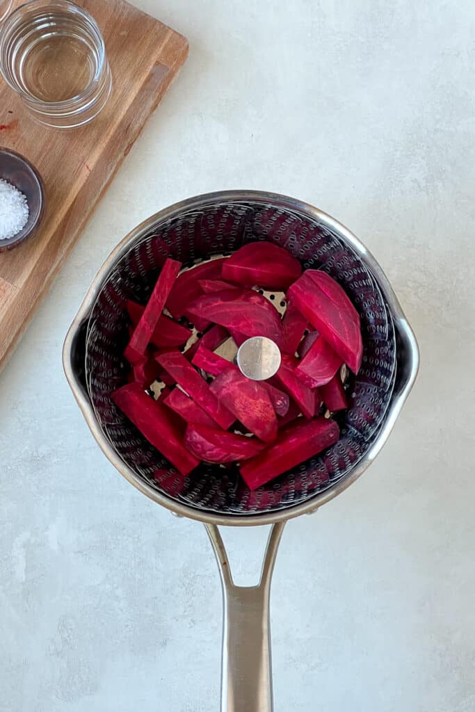 Sliced beets in a pot with a steaming basket.