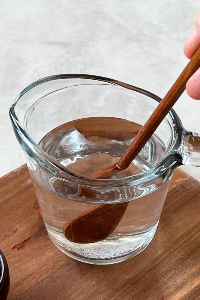 Quick pickle brine mixture in a jug with wooden spoon stirring.