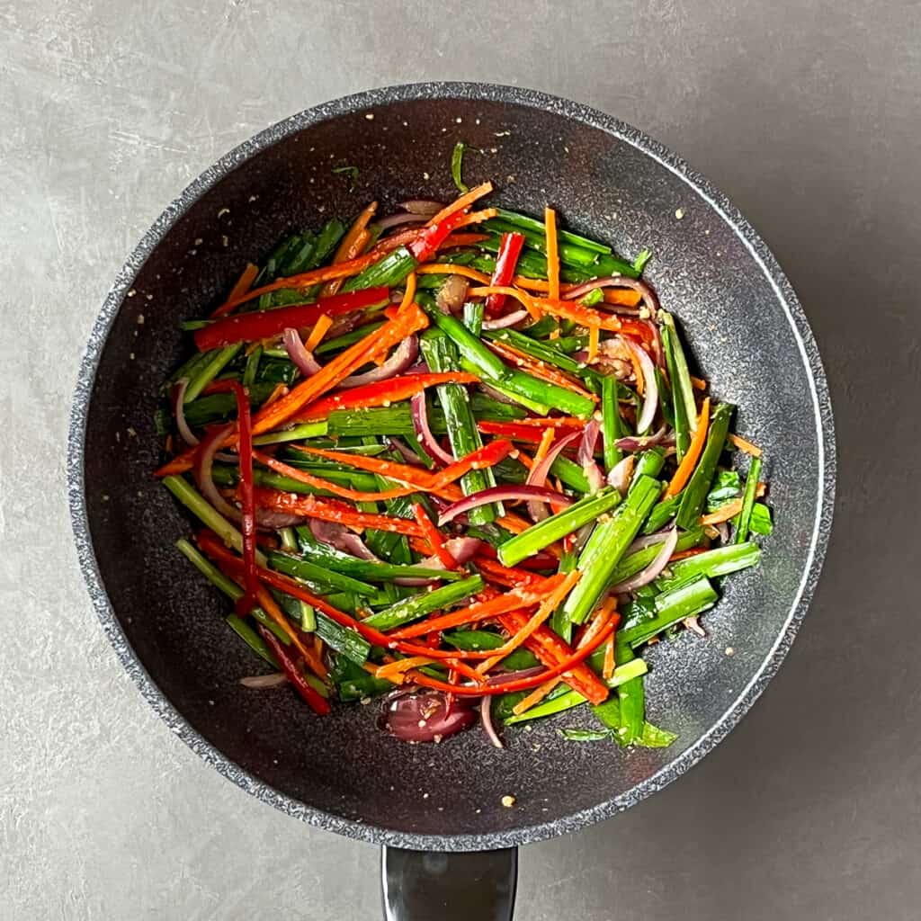 Stir fry vegetables sliced lengthwise in a wok.