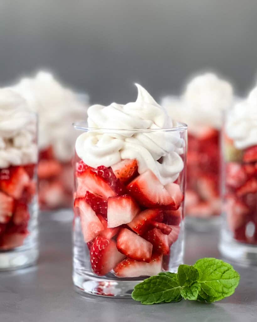 Small glasses with sliced strawberries topped with oat whipped cream.