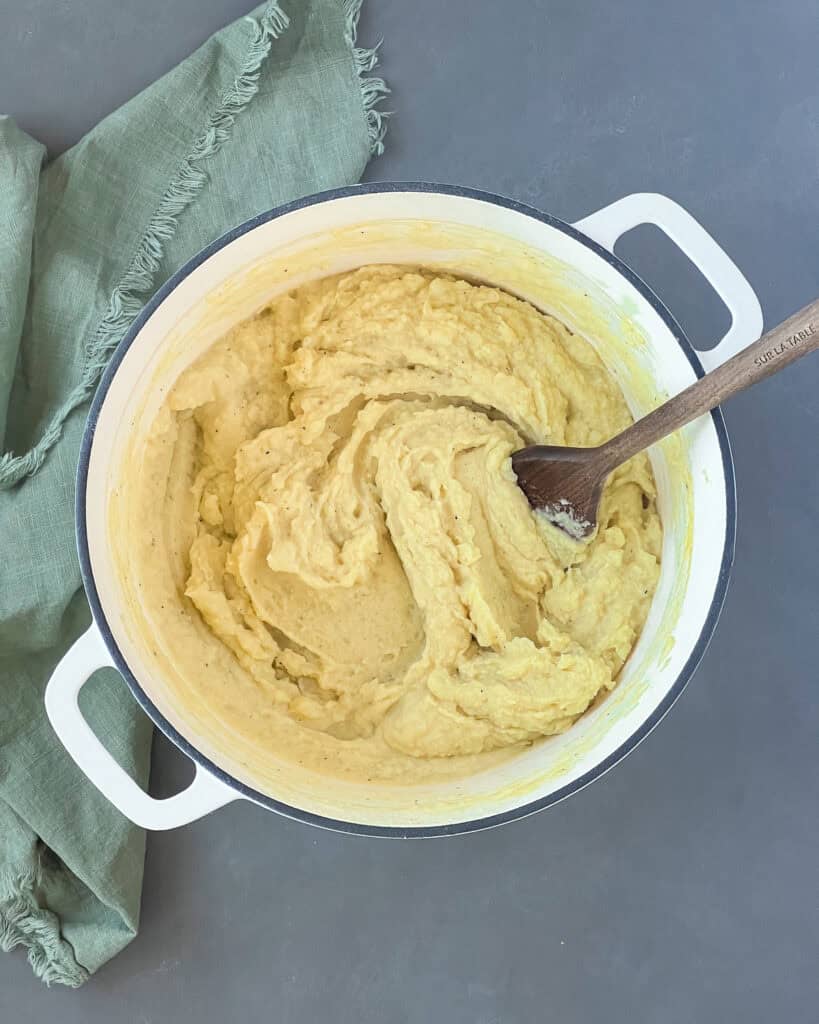 Almond milk mashed potatoes in a dutch oven with a wooden spatula in it.