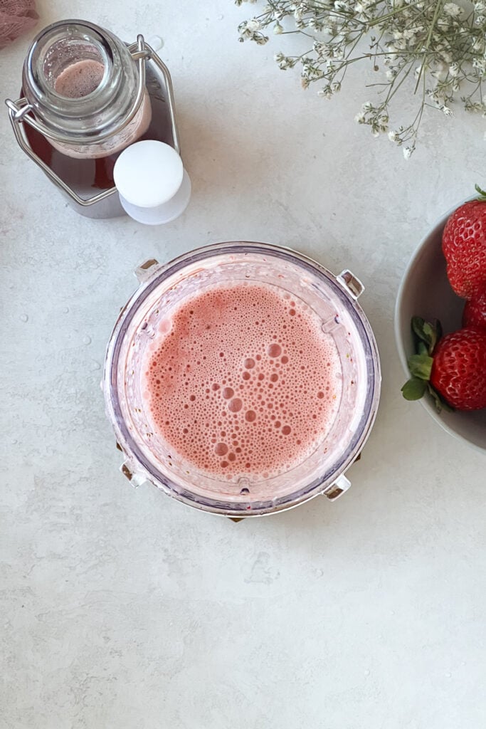 A blend of strawberry milk to in a blender cup.