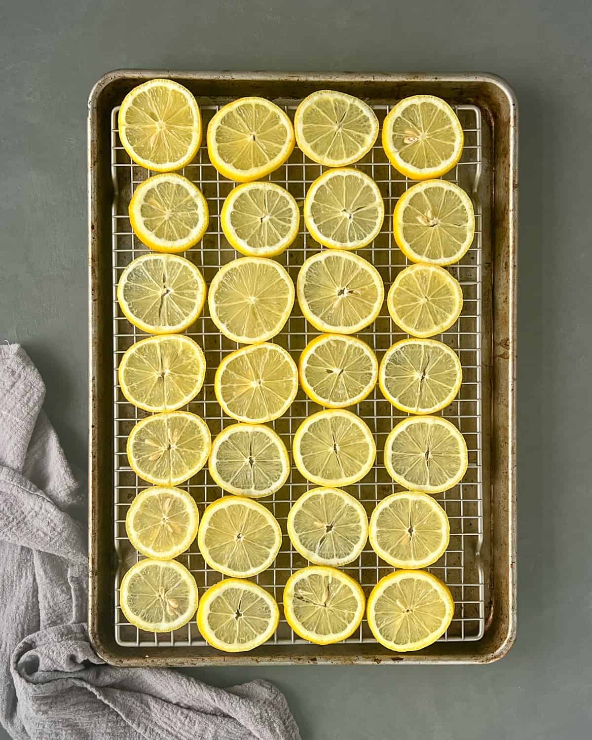Thin lemon slices arranged single layer on a wire cooling rack inside a baking sheet.