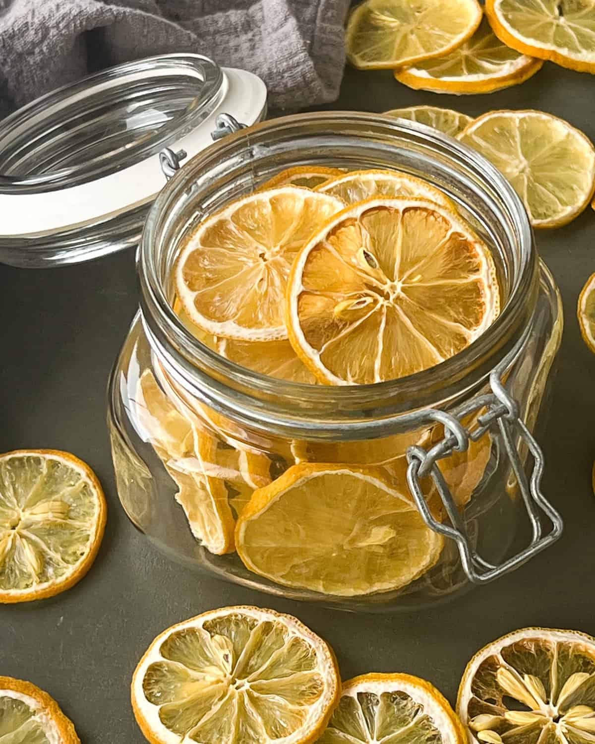 Dried lemon slices in a wide mouth open glass jar and some around the jar.