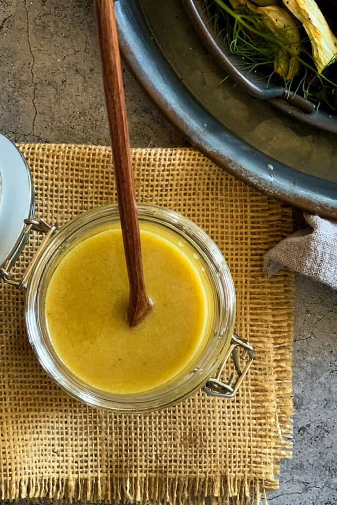 Maple dijon dressing in an open wide mouth glass jar with a wooden spoon in it.
